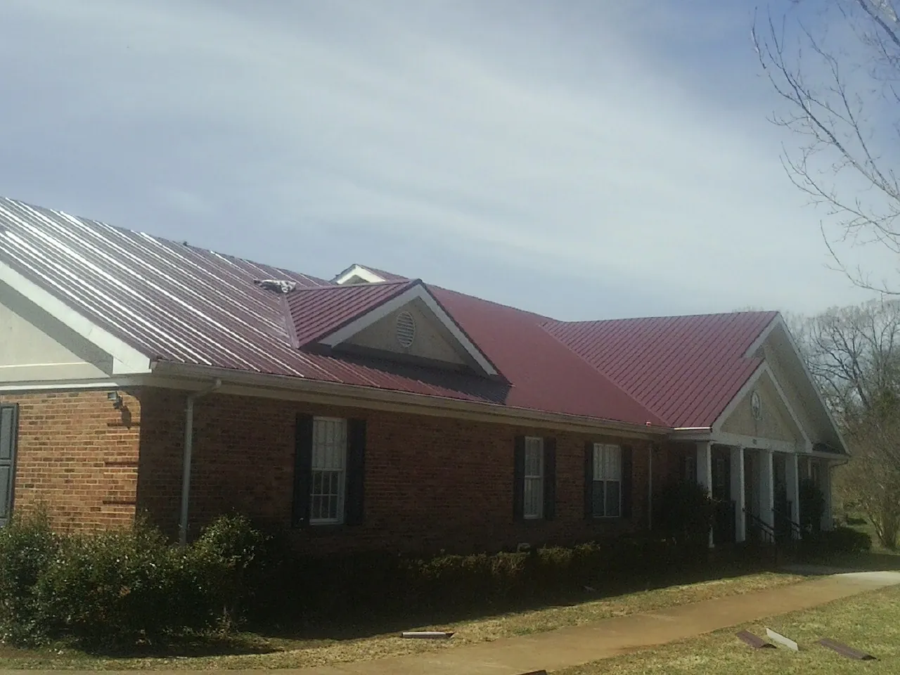 Red metal roof with gabled entries on a long brick building, from a Hail Damage Roof Repair job in Green Bay