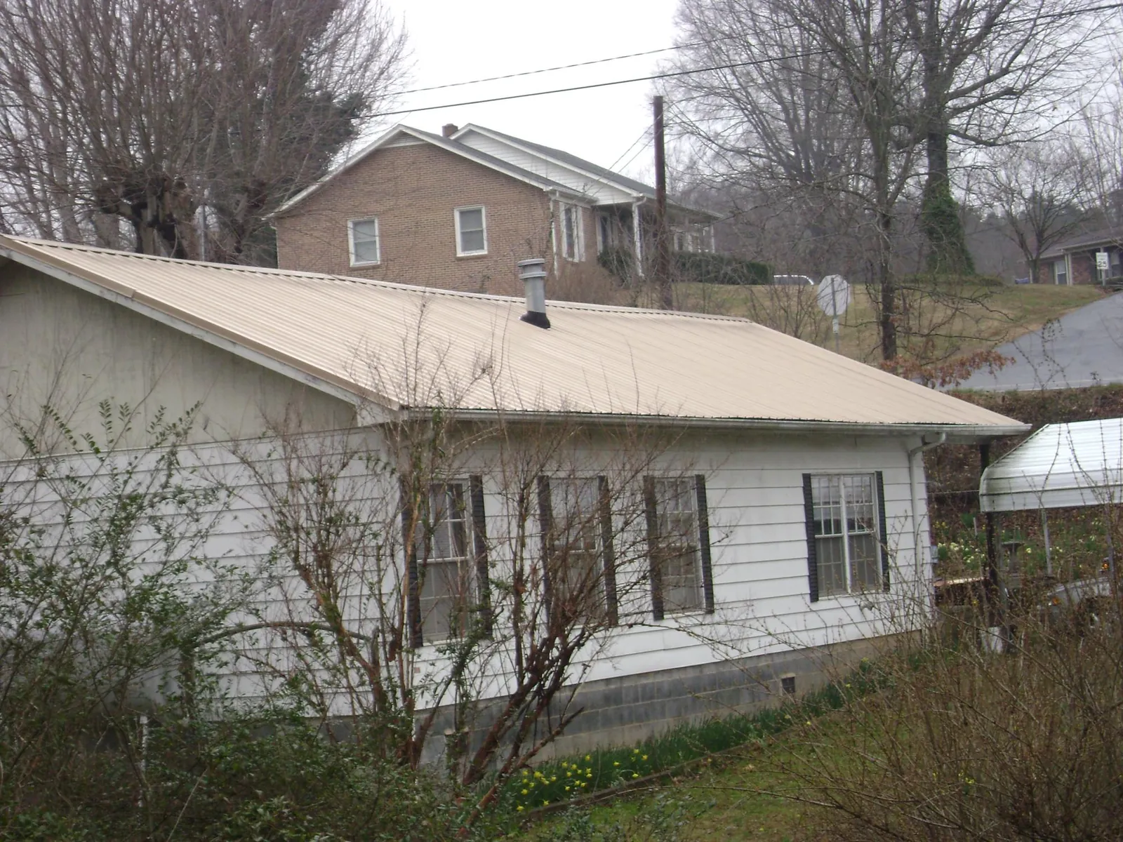 Tan metal roof on a white sided house set into a hillside — Commercial Roofing by Roofing Brothers in Green Bay
